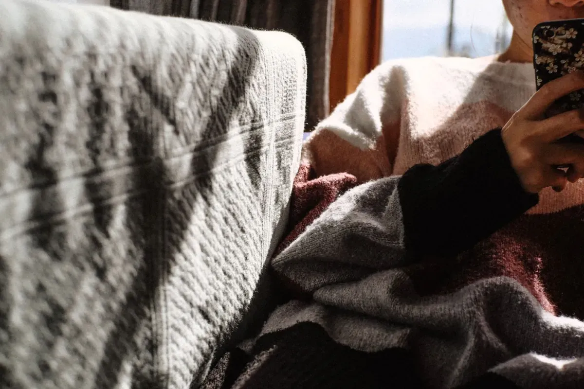 Person in a cozy sweater using a virtual pet app on a smartphone