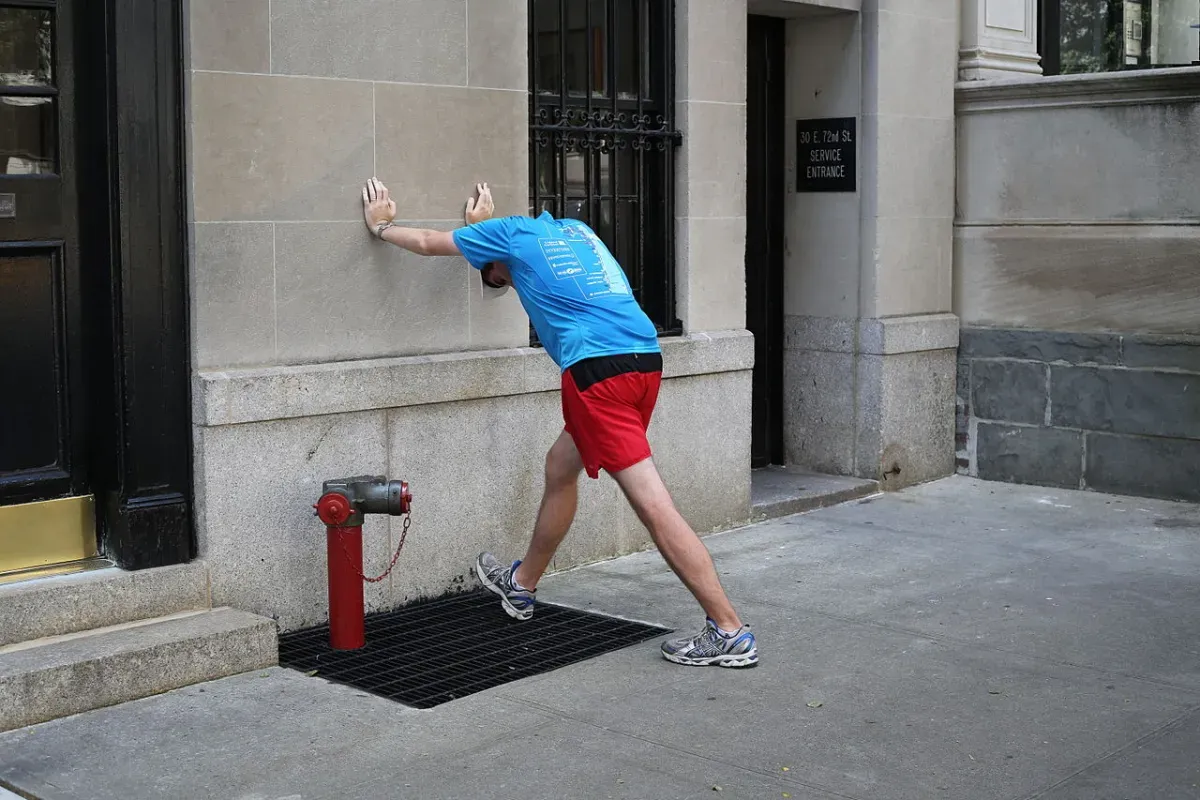 Runner leaning into a wall calf stretch with the back knee straight and heel flat on the ground