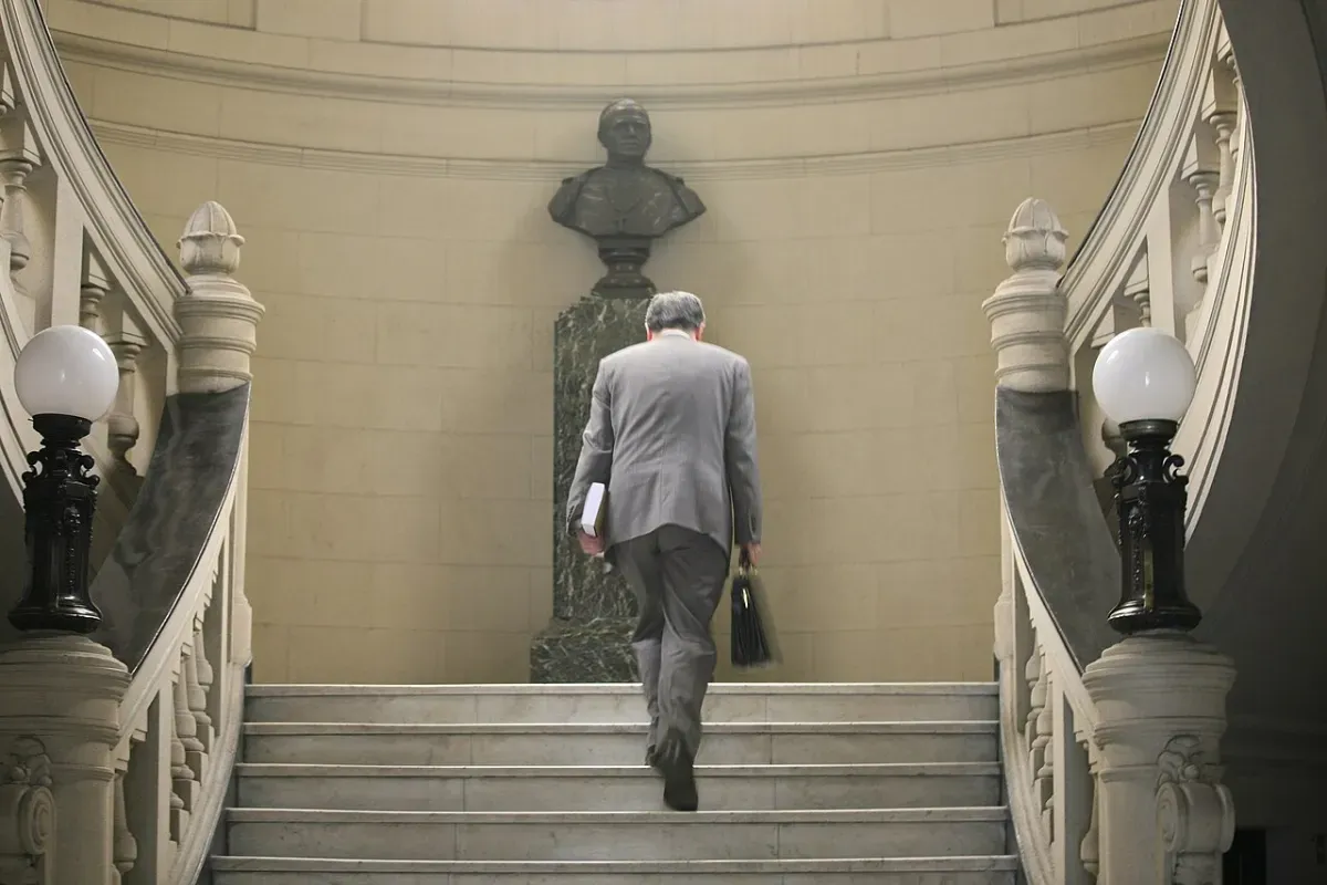 A man in a grey suit carrying a briefcase and a book walks up a marble staircase, the kind of everyday stair climb that turns into a VILPA burst when you take it fast