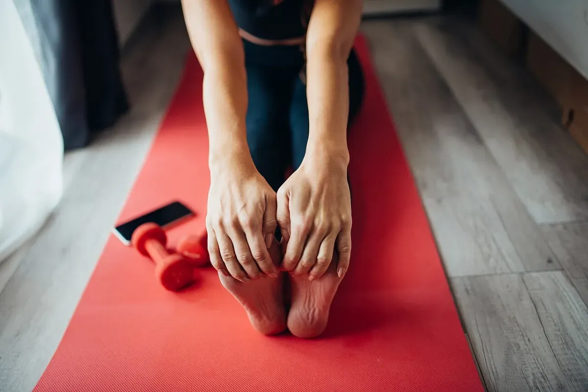 Woman doing a seated full body stretch reaching for her feet at home
