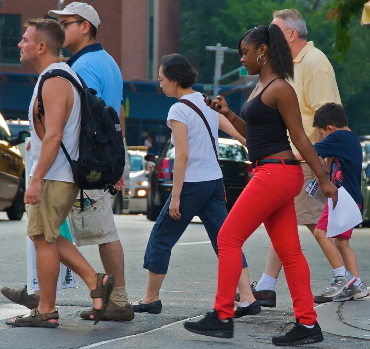 A pedestrian looking at her phone while crossing a busy street, the main safety risk of GPS games