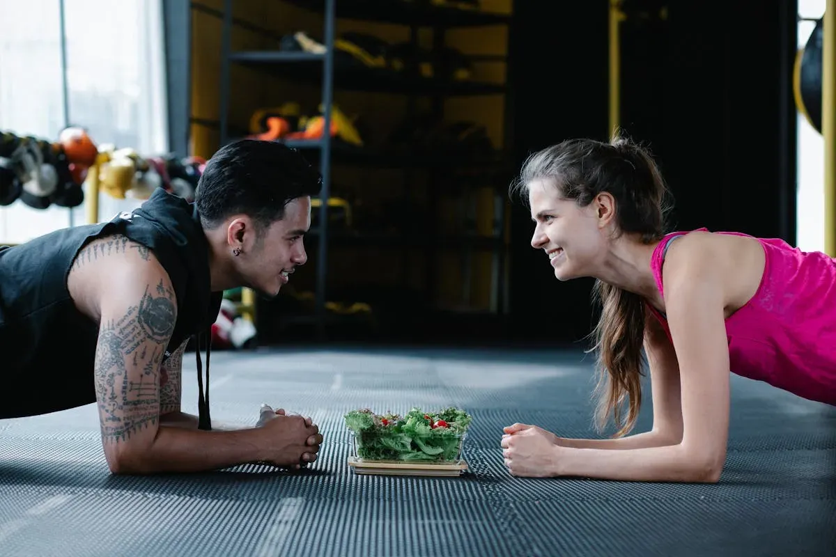 Two gym partners doing a partner plank and smiling at each other