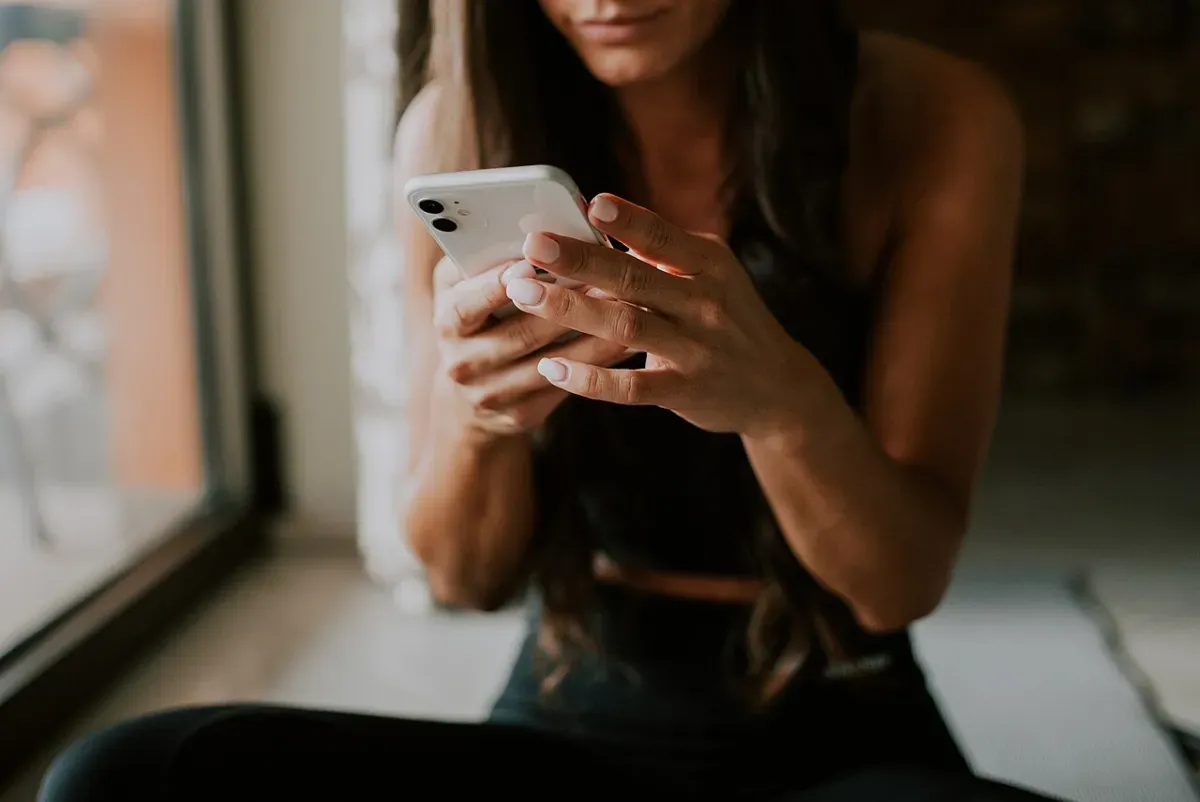 A woman sitting on a yoga mat checking her phone