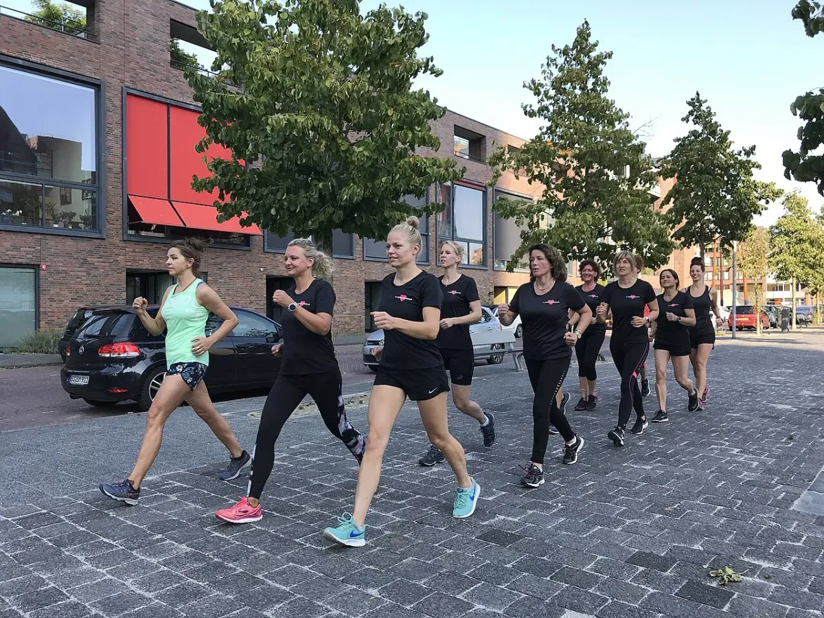 A group of women, most in matching black tops, power walking with bent arms along a paved city street