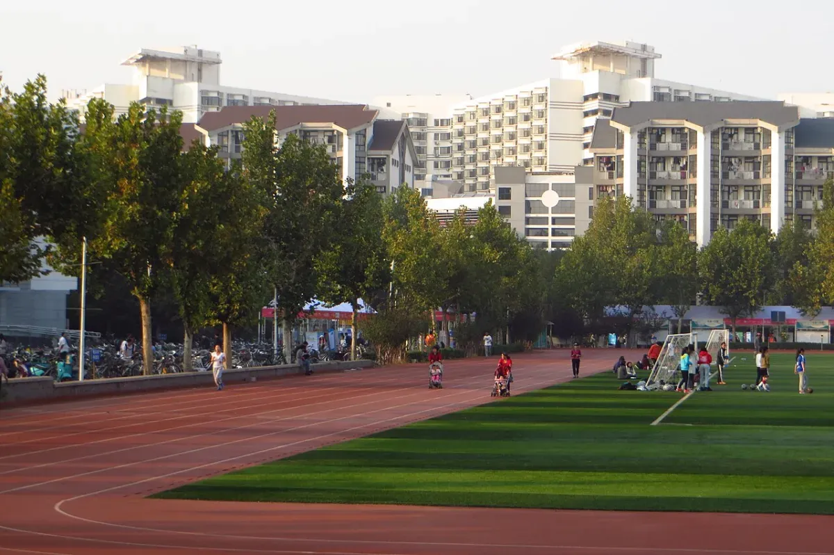 People walking on a red running track beside a green sports field at a university campus