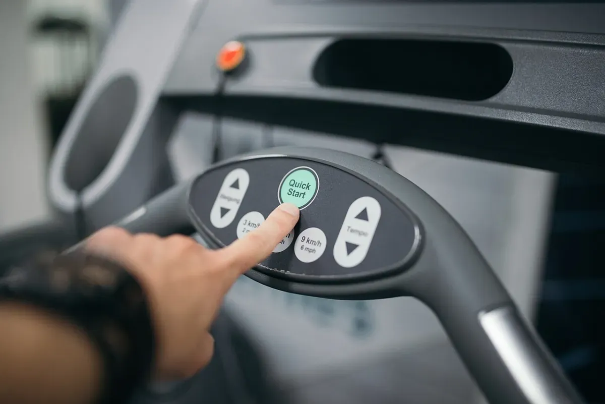 A finger pressing the Quick Start button on a treadmill console with preset speed buttons