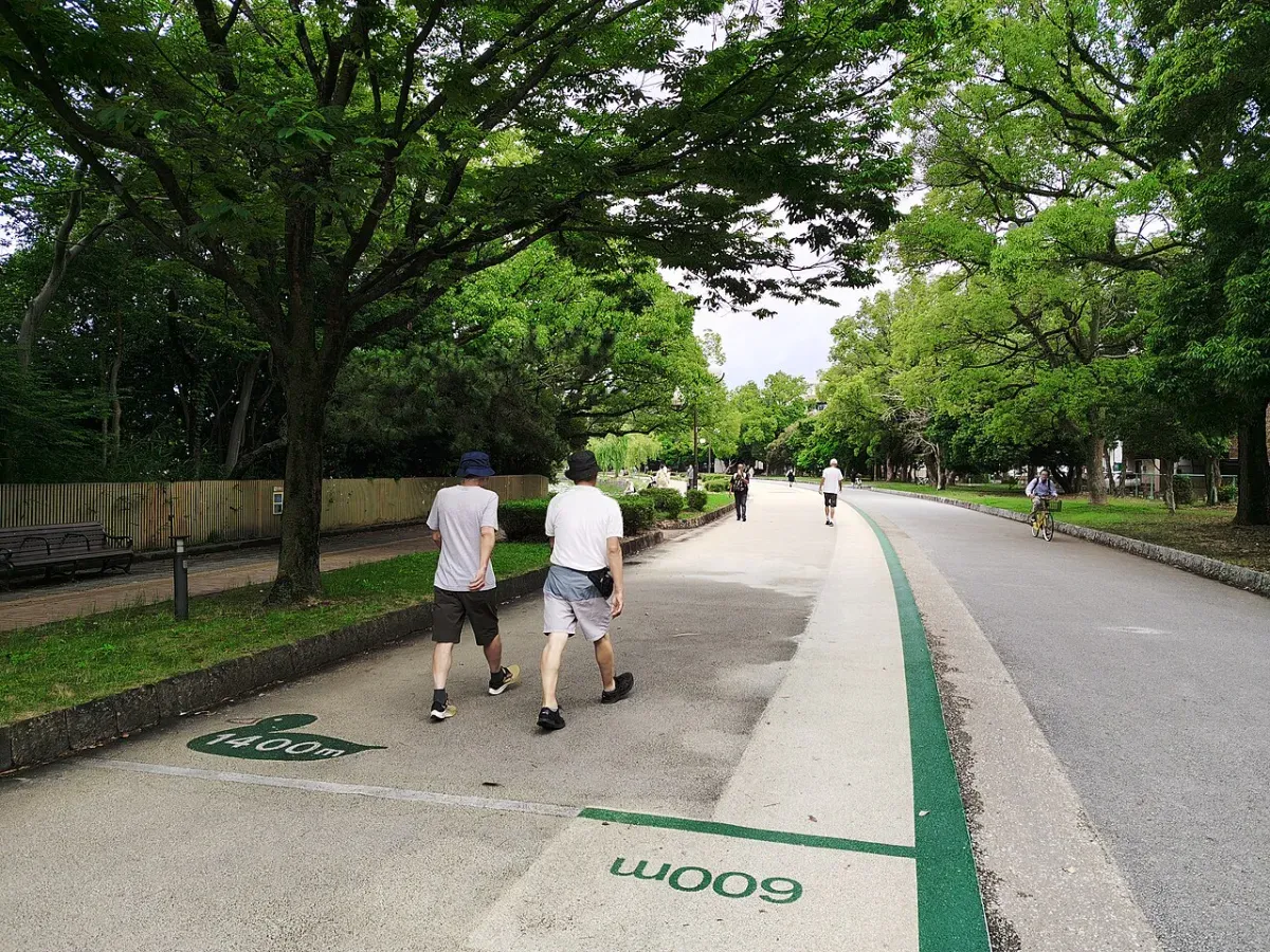 路面に「1400m」「600m」の距離表示がある公園の周回コースを歩く2人（福岡市・大濠公園）