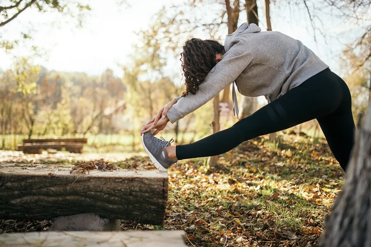 Woman outdoors folding forward over a straight leg propped on a log, stretching the hamstring behind the knee
