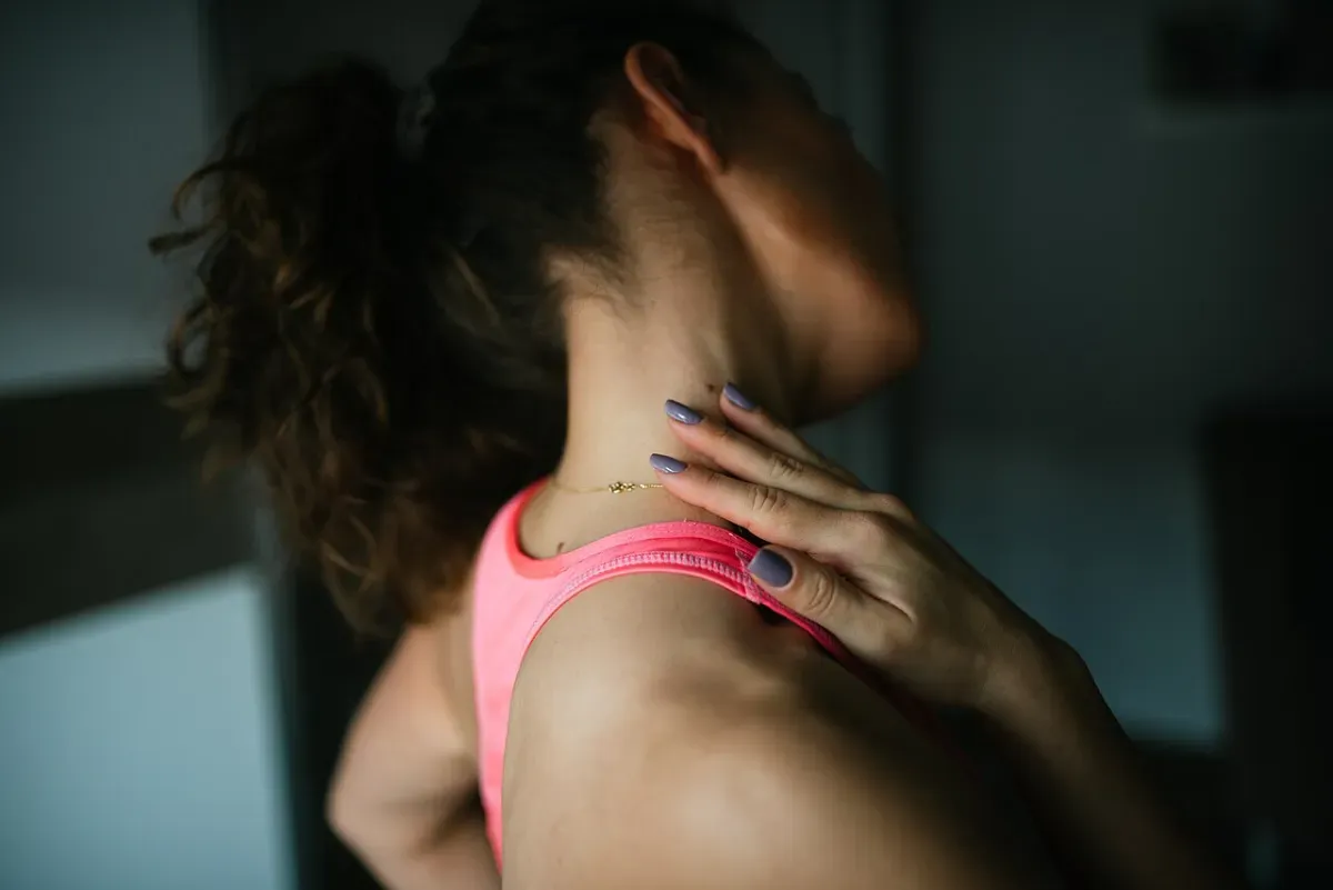 A hand pressed to the base of the neck, where the upper trapezius sits