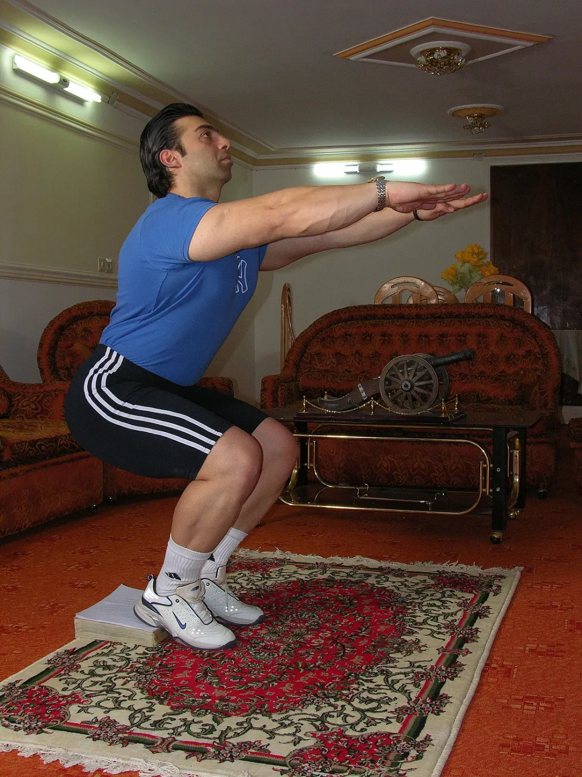 Man at the bottom of a deep bodyweight squat during a leg workout at home