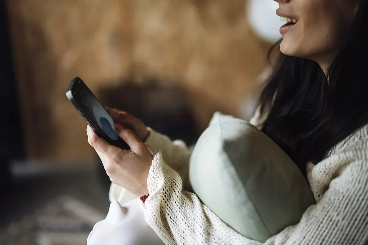 自宅でクッションを抱えながらかわいい習慣化アプリをスマホで開く人