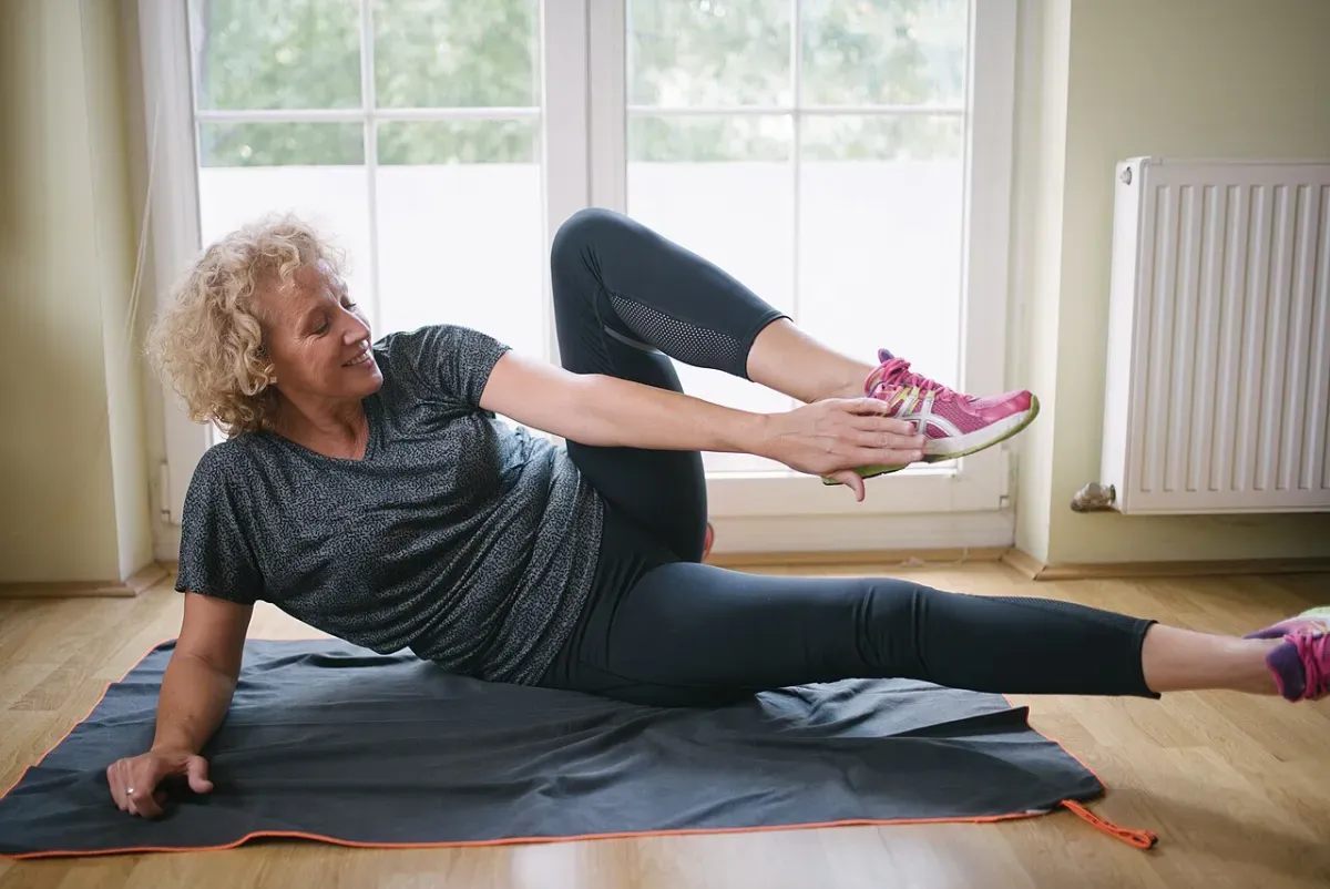 Woman on an exercise mat at home holding a side-lying lower-body stretch in bright natural light