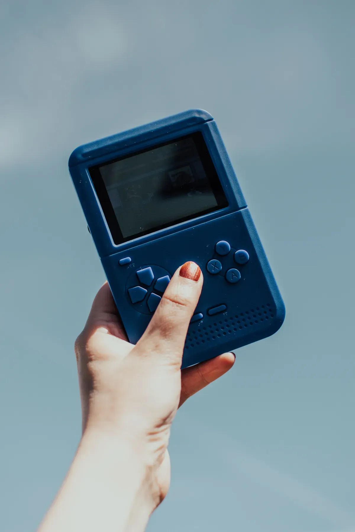 A hand holding a retro handheld game console, the nostalgia behind every Tamagotchi app