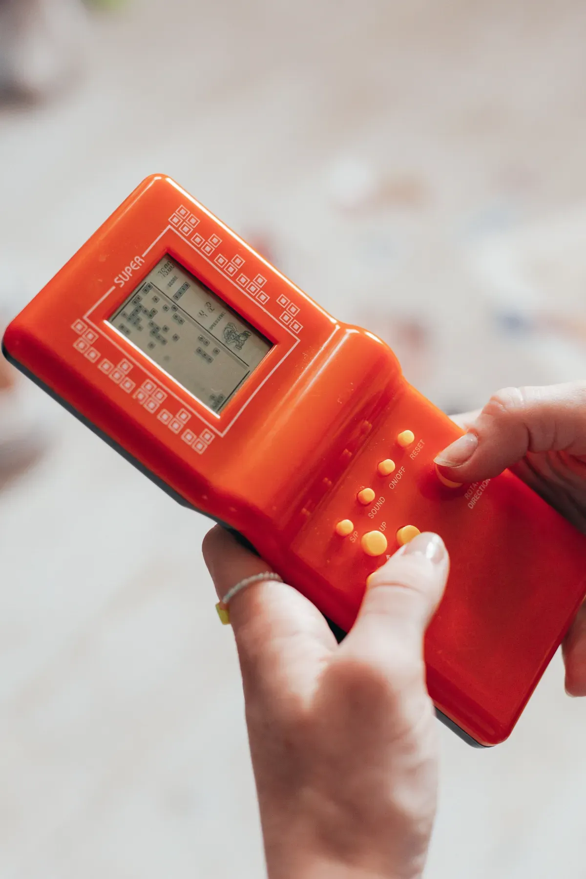 A close-up of hands playing a retro handheld game, the kind of Tamagotchi app nostalgia adults chase