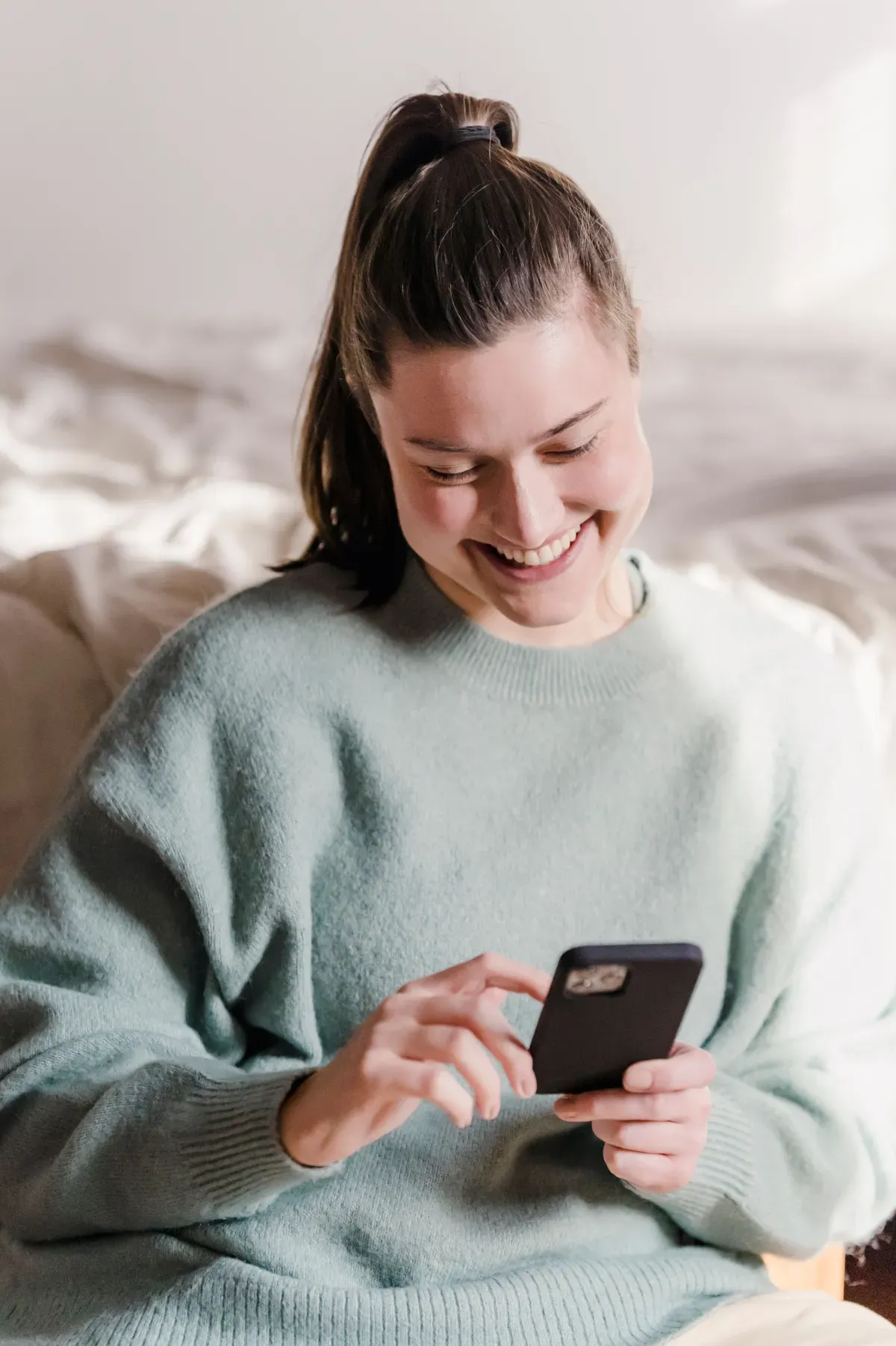 Woman relaxing at home and smiling while using a virtual pet app on her phone