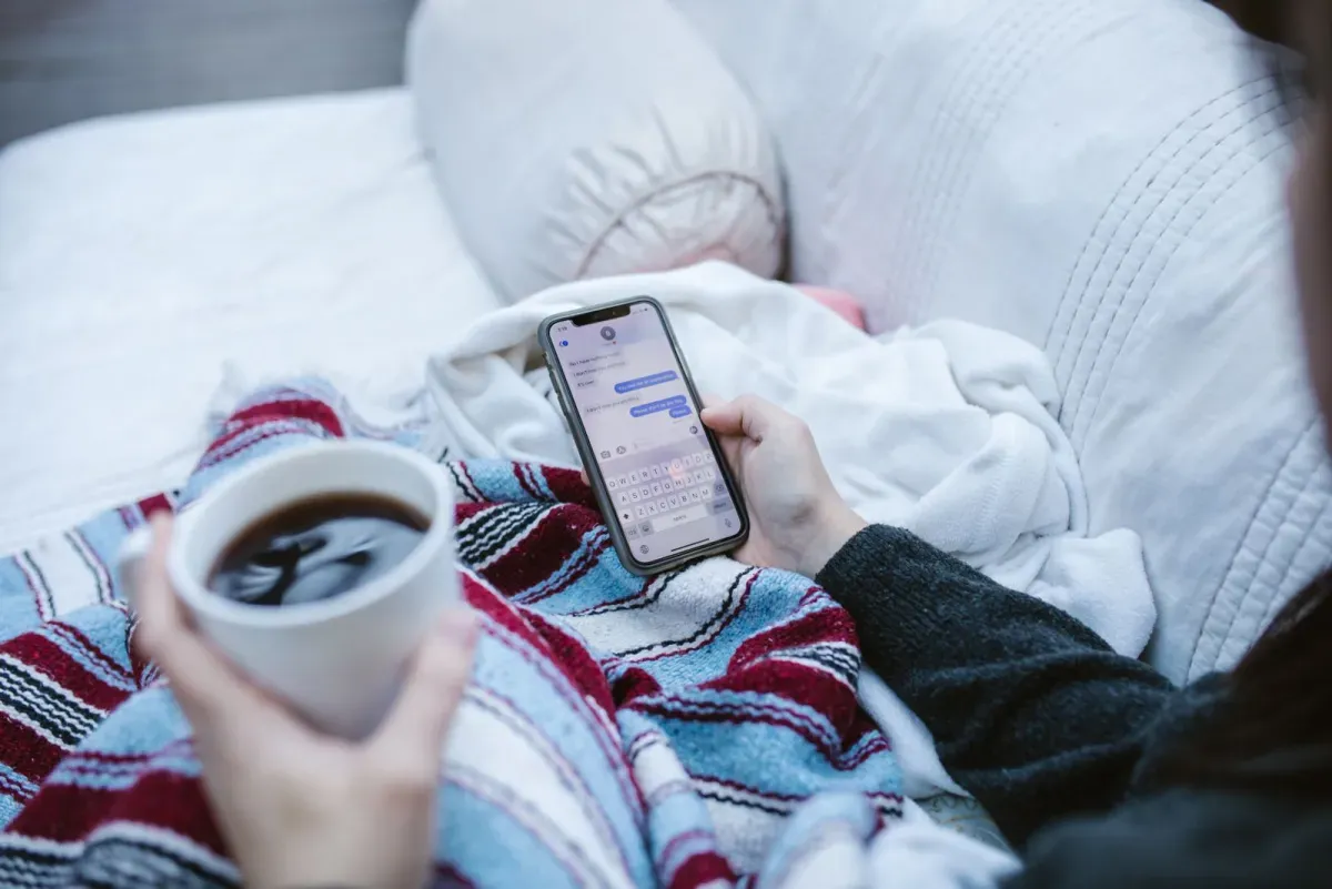 Person relaxing at home with a warm drink while using a phone