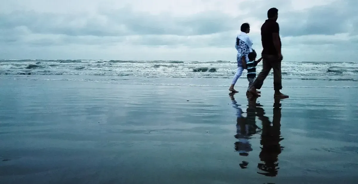 A family walking together along a wet beach under a cloudy evening sky, a relaxed walk after a meal