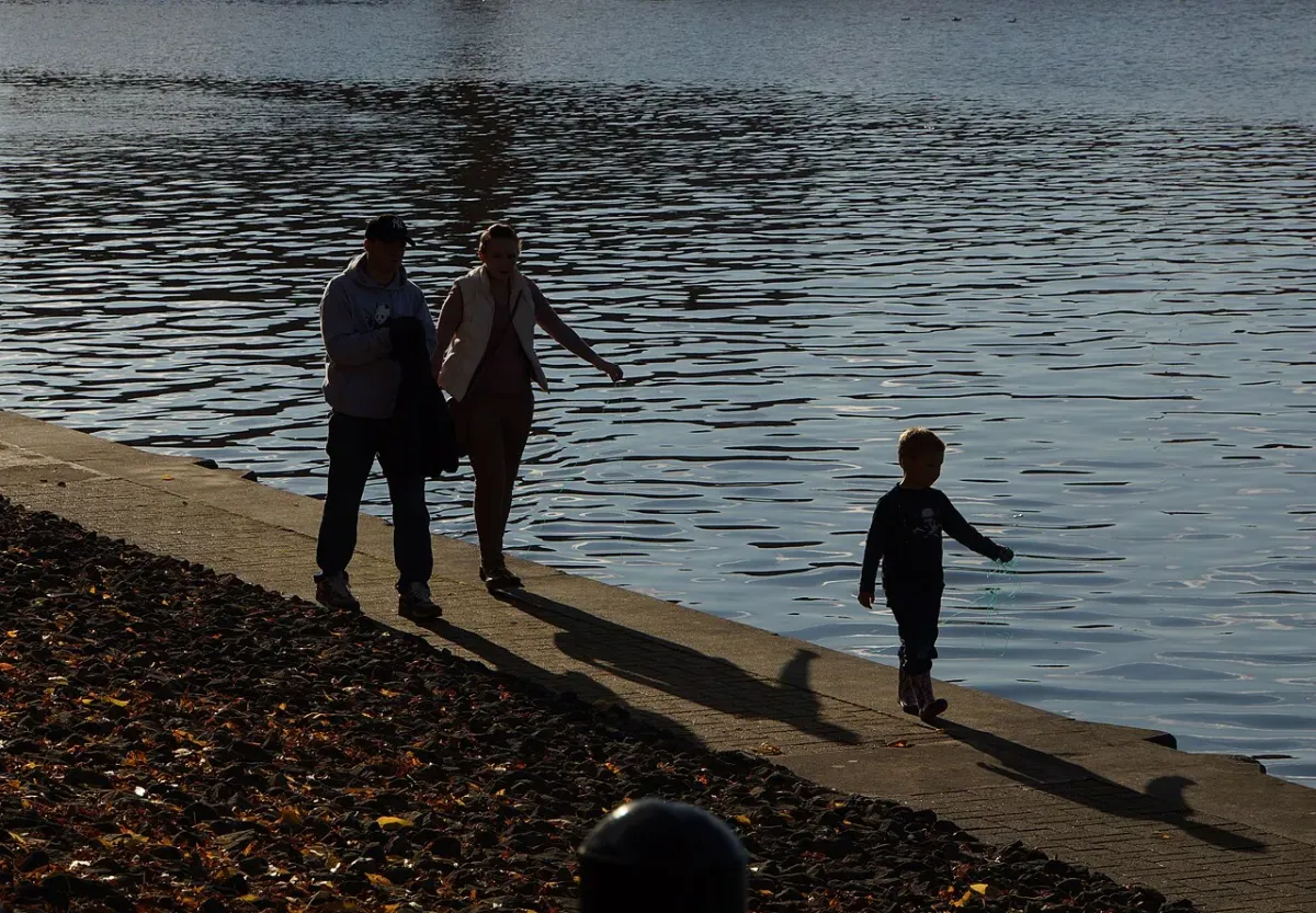 Two adults and a small child walking along a harbourside path in low evening sun, casting long shadows