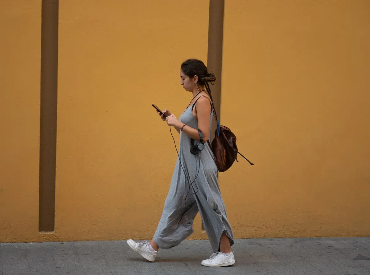 A woman walking down the street with headphones plugged into her phone, following an audio walk