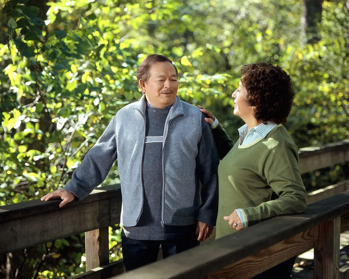 An older couple pausing on a wooden footbridge during a walk in the woods