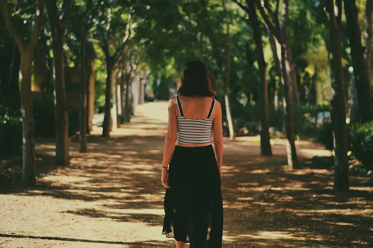 A woman walking alone down a tree-lined park path on an everyday walk