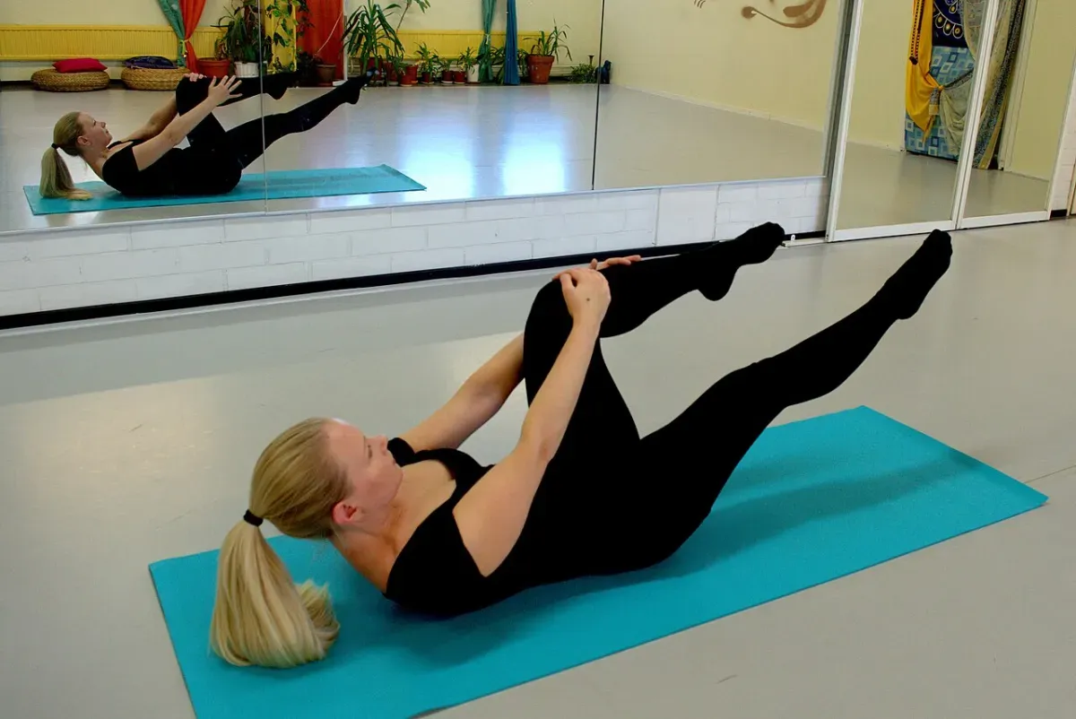 Woman doing a pilates single-leg stretch on a mat with one leg extended